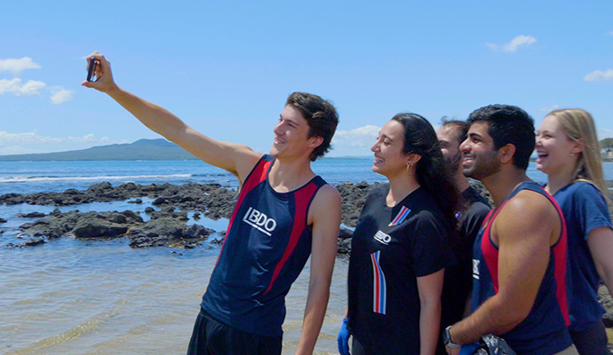 graduates taking a group selfie on the beach