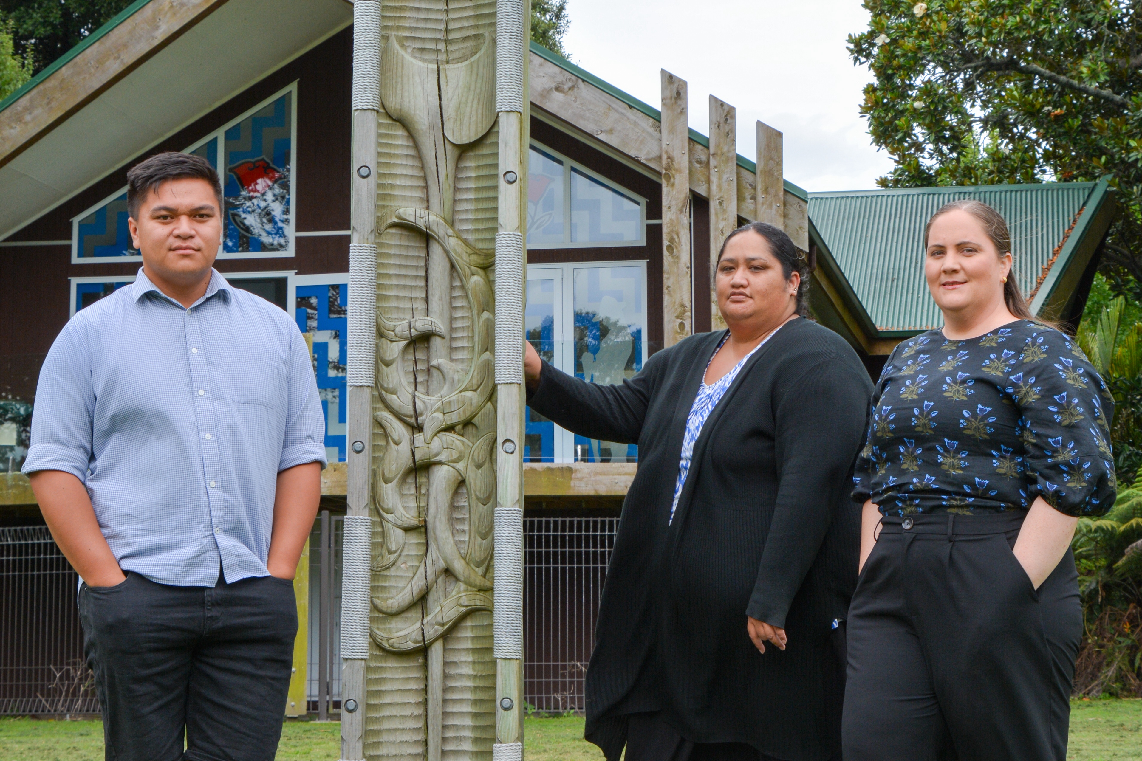 Three people standing outside a marae